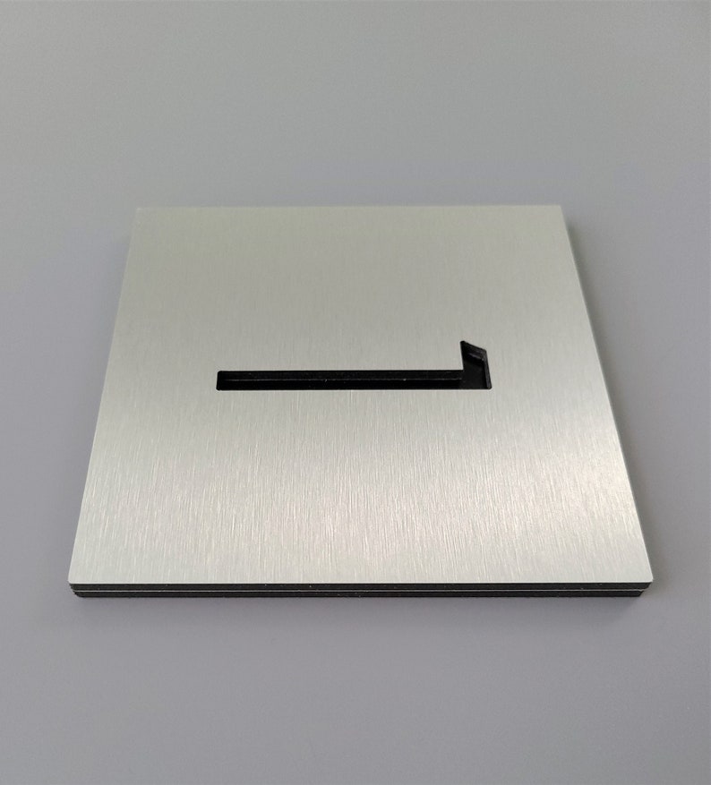 May include: A brushed silver metal sign with a cut-out arrow pointing to the left. The sign is rectangular and has a black border.