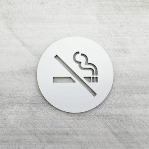 May include: White round sign with a no smoking symbol. The symbol is a cigarette with smoke coming from it, crossed out with a diagonal line.