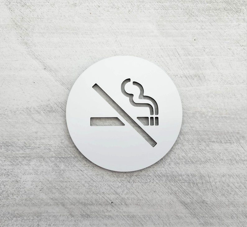 May include: White round sign with a no smoking symbol. The symbol is a cigarette with smoke coming from it, crossed out with a diagonal line.