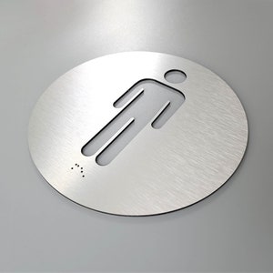May include: A round, silver-colored metal sign with a cutout of a person figure. The sign has braille dots at the bottom.
