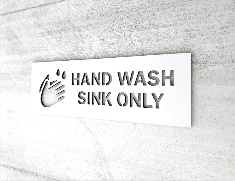 May include: White sign with black text that reads "HAND WASH SINK ONLY". A hand washing icon is to the left of the text.