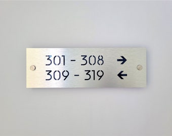 May include: A silver metal sign with black numbers and arrows indicating directions. The sign reads "301 - 308" with a right arrow and "309 - 319" with a left arrow.