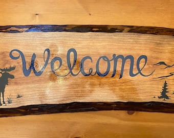 Hand painted welcome sign with moose and pine trees.