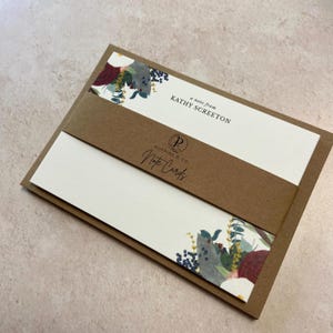 May include: A set of brown and white note cards with a floral design. The cards have a brown band with the text "a note from KATHY SCREETON" and "Poypings & Co. Note Cards".