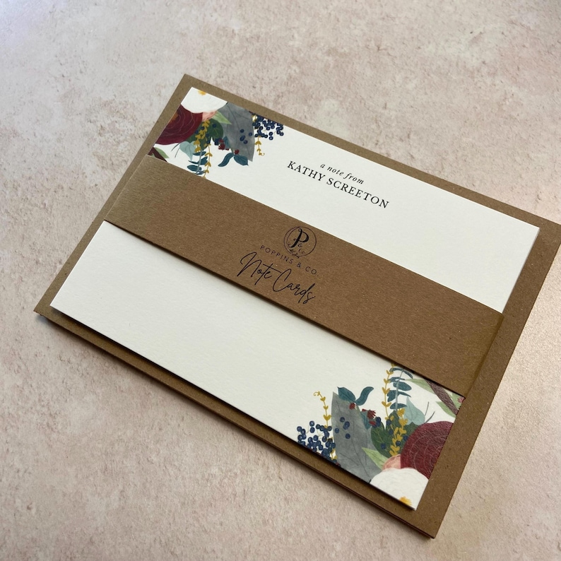 May include: A set of brown and white note cards with a floral design. The cards have a brown band with the text "a note from KATHY SCREETON" and "Poypings & Co. Note Cards".