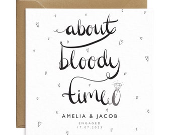 May include: A white engagement card with the phrase "about bloody time" in black script. The card features a diamond ring illustration and small heart doodles. The names Amelia & Jacob and the engagement date are also printed.