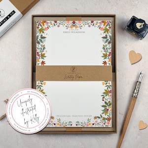 May include: A boxed stationery set with white writing paper, floral border, and a pen. The set includes ink and a sticker that reads "Uniquely Illustrated by Kelly". The writing paper is personalized with a name and address.
