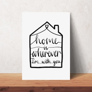 May include: A white rectangular print with a black outline of a house. The words "home is wherever I'm with you" are written in a handwritten style inside the house outline. A heart is at the top.