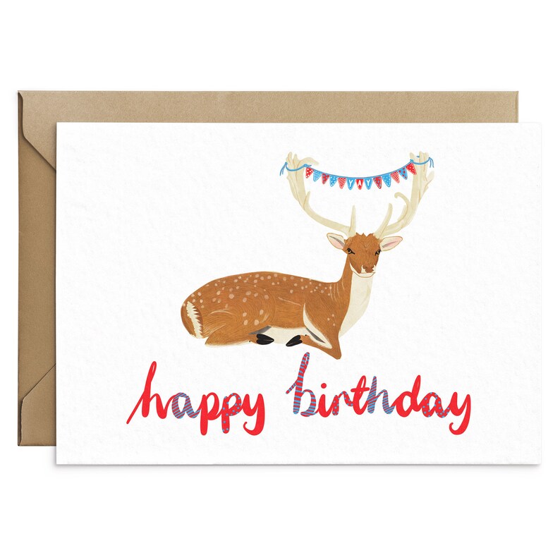 May include: A white card with a brown envelope. The card features a cartoon deer with a red and blue bunting over its antlers. The text "happy birthday" is written in red and blue.