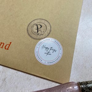May include: A brown paper envelope with two circular stickers. One sticker has a circular design with the letters "P & Co." The other sticker says "Happy things within" in cursive, surrounded by a pink border.