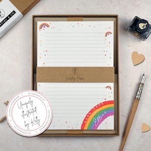 May include: A stationery set with lined writing paper decorated with rainbows and stars. The set includes a pen, ink, and a decorative sticker. The writing paper has the text "Writing Paper" and "with love from Ellie". The set is packaged in a brown box.