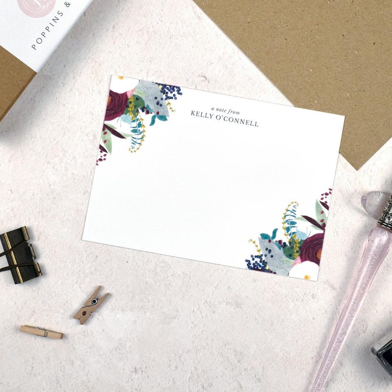 May include: A white card with a floral design in shades of blue, purple, and green. The text "a note from KELLY O'CONNELL" is printed in black at the top of the card.