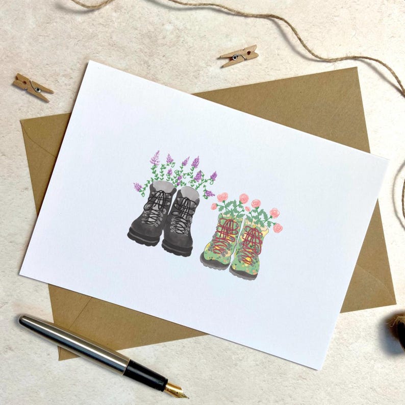May include: A greeting card featuring an illustration of two pairs of hiking boots filled with flowers. One pair is gray with purple flowers, and the other is green with pink flowers. The card is on a white background.