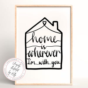 May include: A framed art print with a minimalist design. The black line art features a house outline with the words "home is wherever I'm with you" in a handwritten style. A circular logo is in the lower left corner.
