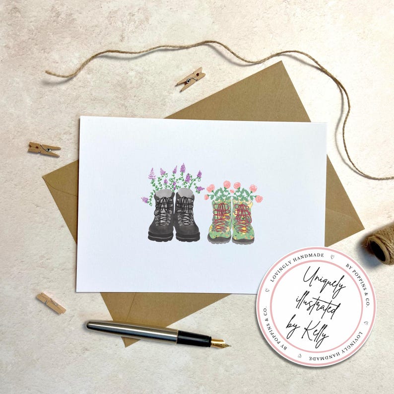 May include: A greeting card featuring watercolor illustrations of hiking boots filled with flowers. One pair is black, the other green. The card is on a white background, with a brown envelope, pen, and a sticker that says "Uniquely illustrated by Kelly."