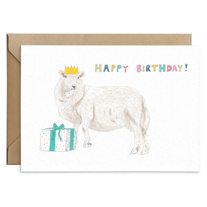 May include: A white sheep wearing a yellow crown and holding a gift box with a blue and white polka dot pattern. The text "HAPPY BIRTHDAY!" is written in colorful letters above the sheep.