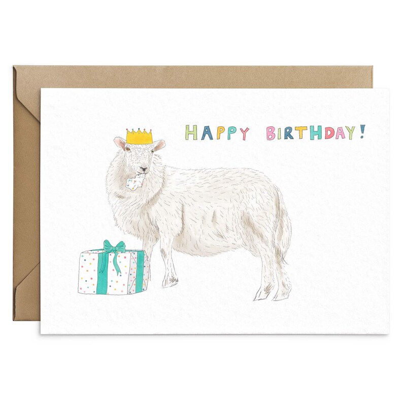 May include: A white sheep wearing a yellow crown and holding a gift box with a blue and white polka dot pattern. The text "HAPPY BIRTHDAY!" is written in colorful letters above the sheep.