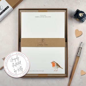 May include: A stationery set with white writing paper, featuring the text "a letter from EMMA LOUISE MALONE". The set includes a watercolour illustration of a robin. Packaged in a brown box with a matching band.
