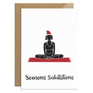 May include: A white greeting card with a black silhouette of a person in a yoga pose, wearing a Santa hat, on a red mat. The text "Seasons Salutations" is written in black script below the image. The card is inside a brown envelope.