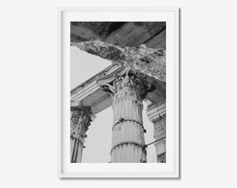 May include: Black and white framed print featuring a low-angle view of ancient Roman columns. The columns have ornate carvings and are set against a bright sky. The print is in a white frame, suitable for home decor.