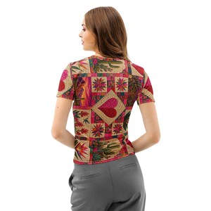 May include: A short-sleeve t-shirt featuring a multi-colored patchwork design with repeating squares. The pattern includes images of cacti, starburst shapes, and a prominent central heart motif in shades of red, pink, gold, and green.