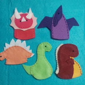 May include: Five felt finger puppets shaped like dinosaurs. The puppets are red, orange, green, purple, and brown.
