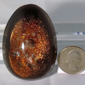 Può includere: Un uovo di resina di colore marrone scuro, di forma ovale, con un interno scintillante di colore rame. Il glitter è sparso in tutto l'uovo, creando un effetto vorticoso. L'uovo è circa delle dimensioni di una moneta da un euro.
