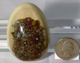 May include: A clear egg-shaped resin paperweight with a mixture of small, colorful, and sparkly stones inside.