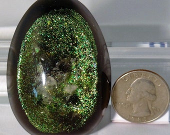 May include: A dark gray egg-shaped glass paperweight with a green glitter and white crystal design inside.
