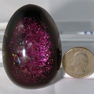 Può includere: Un fermacarte in resina di colore viola scuro a forma di uovo con glitter e scaglie iridescenti incorporati.