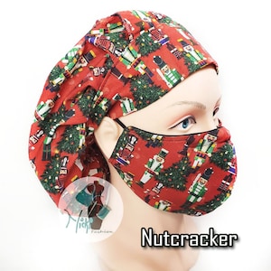 May include: Red fabric scrub cap and face mask set with a repeating pattern of nutcrackers and Christmas trees. The text "Nutcracker" is displayed in a black font. The set is designed for medical professionals.