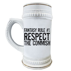 May include: White ceramic beer stein with a gold rim and a black graphic that reads "Fantasy Rule #1 Respect the Commish".