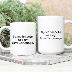 May include: Two white coffee mugs with black text. The text on the mugs reads "Spreadsheets are my love language."