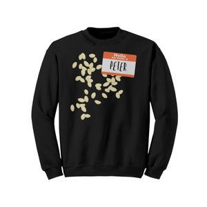 May include: Black sweatshirt with a name tag that reads "Hello my name is PETER". Scattered around the sweatshirt are several off-white, oval-shaped objects. The sweatshirt is a solid black color.
