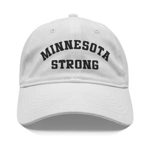 May include: A white baseball cap with a curved brim. The cap features the text "MINNESOTA STRONG" in bold, black letters across the front. The hat is made of a soft fabric and has a classic, adjustable design.