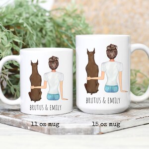 May include: Two white ceramic mugs with a brown dog and a woman with brown hair sitting back to back. The text "Brutus & Emily" is printed on both mugs. The mug on the left is 11 oz and the mug on the right is 15 oz.