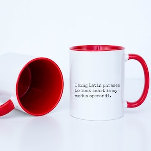 May include: White ceramic mug with a red rim and handle. The mug has black text that reads "Using Latin phrases to look smart is my modus operandi."