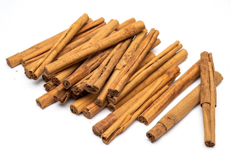 May include: A pile of brown cinnamon sticks on a white background. The sticks are arranged in a random pattern, with some of them overlapping.