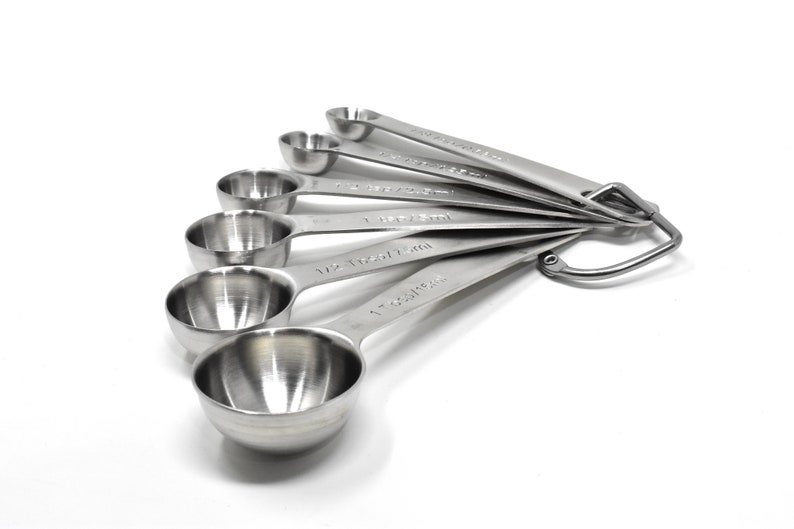 May include: A set of six stainless steel measuring spoons with a hanging loop. The spoons are labeled with measurements in both teaspoons and tablespoons.