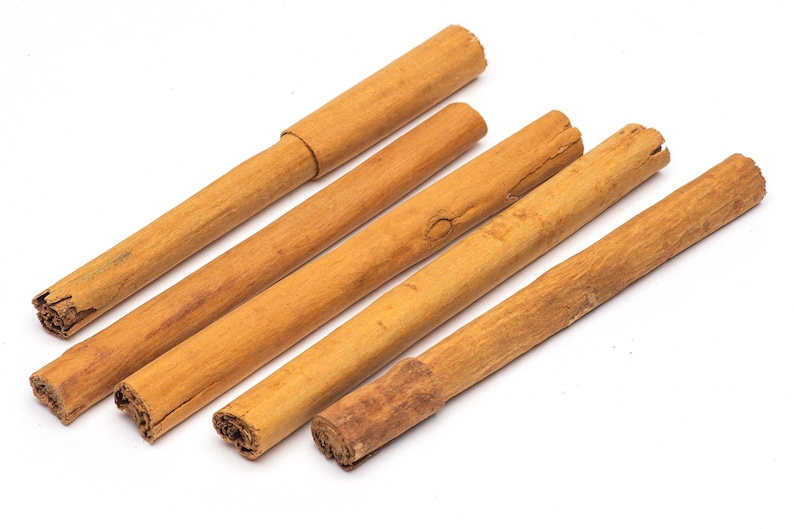 May include: Five brown cinnamon sticks on a white background.