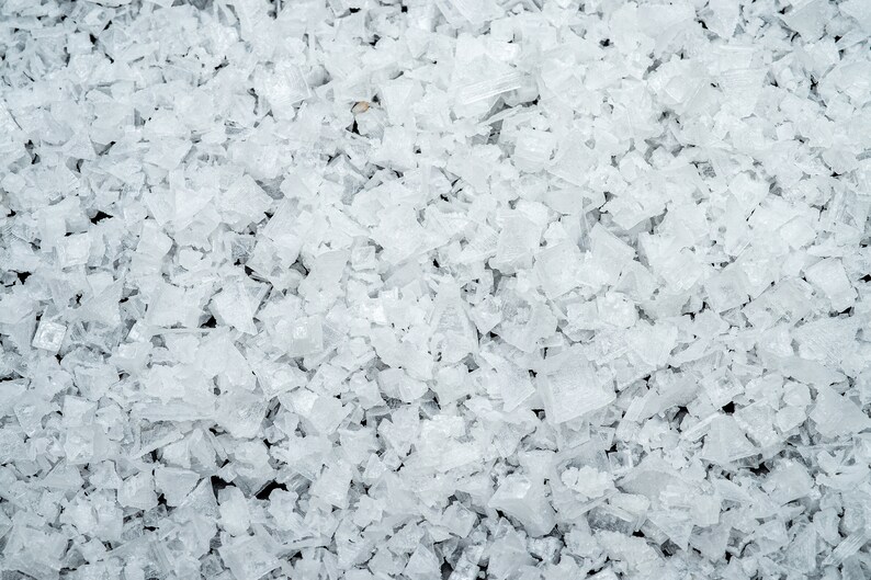 May include: Close-up of a pile of white, translucent, irregularly shaped salt crystals.