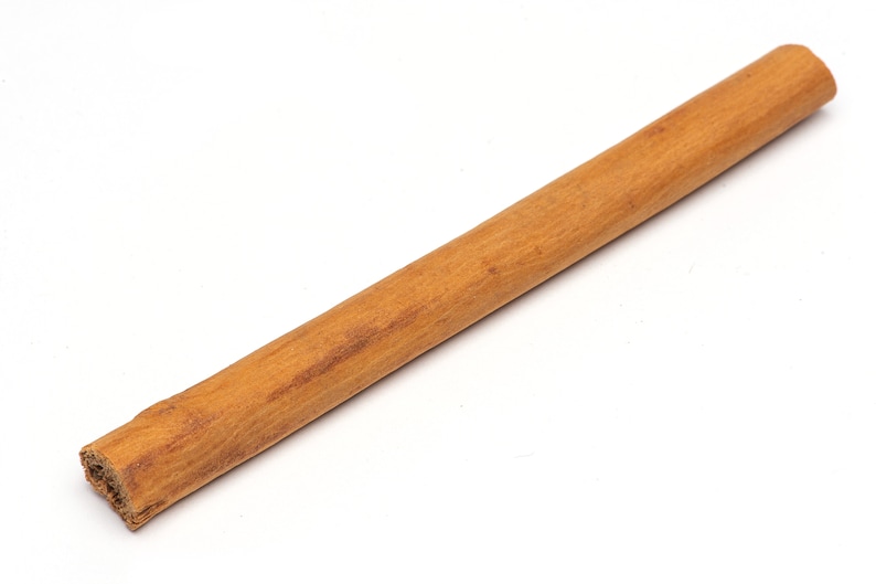 May include: A single cinnamon stick, brown in color, with a rough texture. The stick is lying on a white surface.