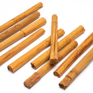May include: A collection of ten brown cinnamon sticks arranged in a random pattern on a white surface.