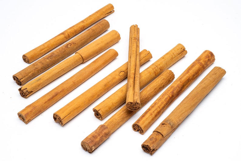 May include: A collection of ten brown cinnamon sticks arranged in a random pattern on a white surface.