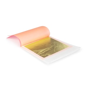 May include: A book of gold leaf, with a single sheet of gold leaf partially unfolded. The gold leaf is a bright, shiny gold color. The book is made of a thin, white paper with a pink backing.