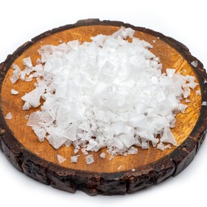 May include: A close-up of a wooden round board with a pile of white sea salt crystals on top.