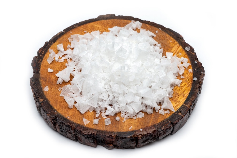 May include: A close-up of a wooden round board with a pile of white sea salt crystals on top.