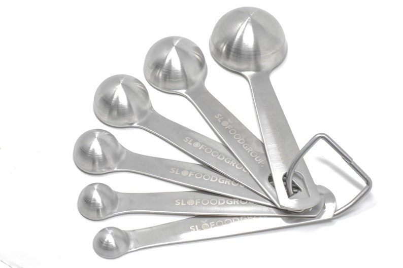 May include: A set of five stainless steel measuring spoons with a ring handle. The spoons are labeled "SLOFOODGROUP".