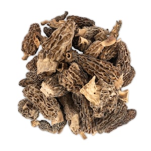 May include: A close-up of a pile of dried morel mushrooms. The mushrooms are brown and have a honeycomb-like texture.