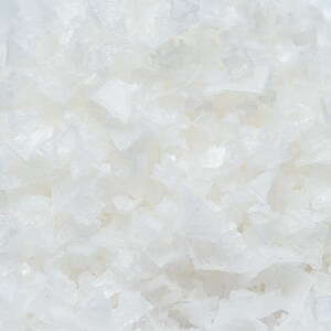 May include: Close-up of white sea salt crystals. The salt is coarse and flaky, with a slightly grainy texture.